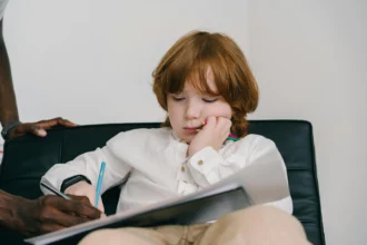 A child sitting thoughtfully with a notebook, while an adult provides support