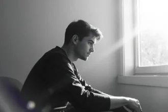 Adult with autism sitting alone, gazing out a window with sunlight streaming in.