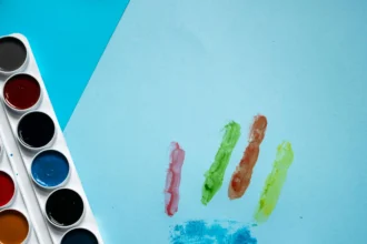 Colorful handprint painted with watercolors next to a palette and Scrabble tiles spelling 'AUTISM' on a blue background.