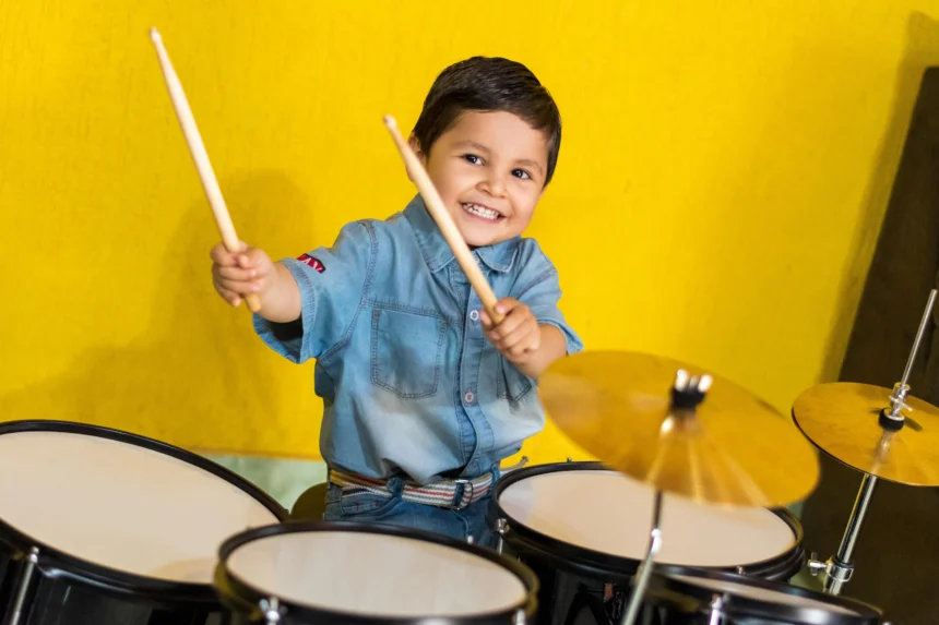 A happy young boy playing the drums with enthusiasm, holding drumsticks in both hands.